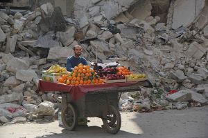Un venditore di frutta siriano attende per i clienti accanto a un edificio danneggiato il 24 febbraio 2014 nel quartiere Shaar della città settentrionale di Aleppo.
